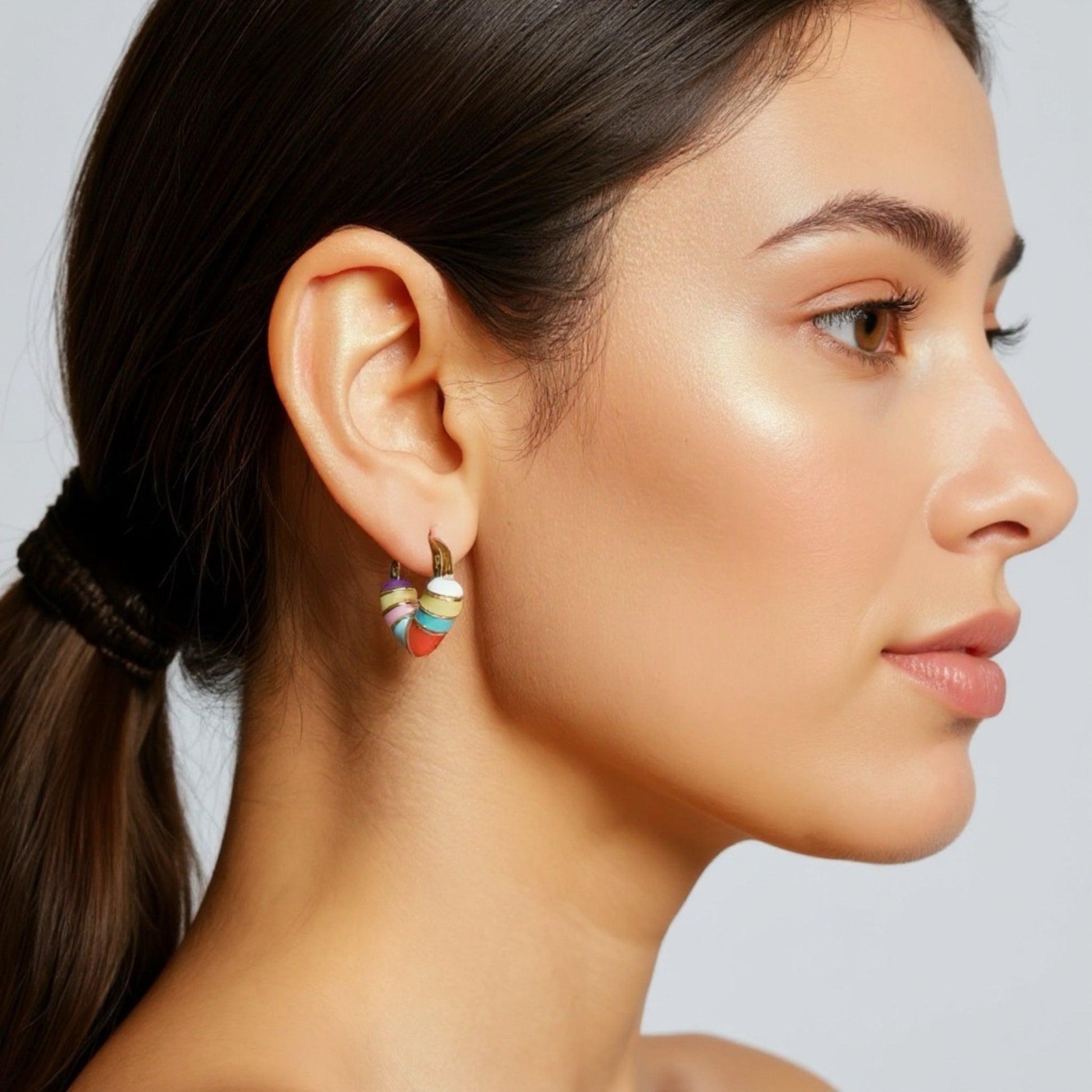 Woman wearing Capri Candy Stripe pastel enamel heart-shaped gold hoop earrings